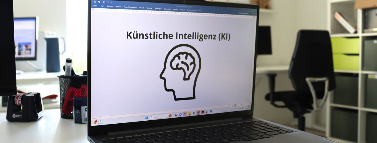 Bild von einem Laptop mit dem Schirftzug Künstliche Intelligenz und einem Kopf mit Gehirn